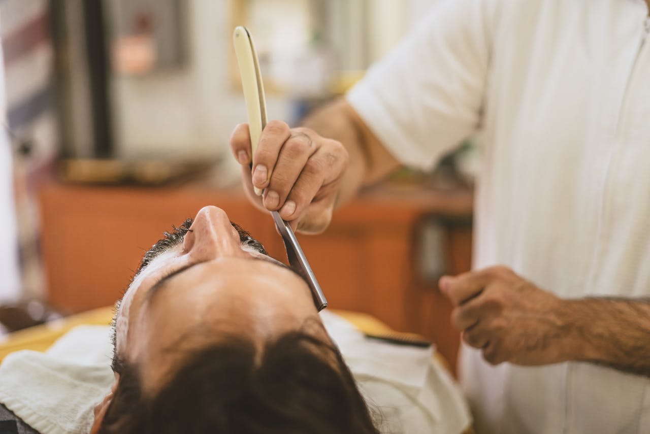 A man receiving a close shave with a straight razor in a classic barber shop setting.