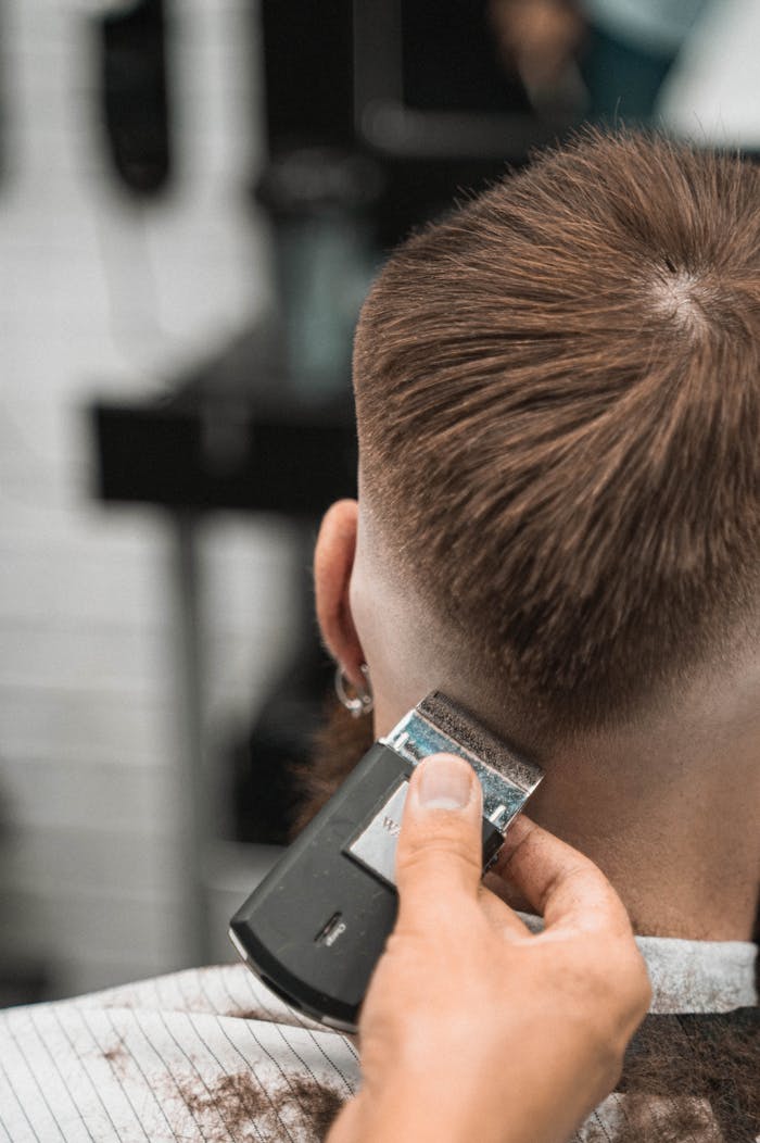Close-up view of a hairstylist creating a haircut with clippers on a man's neck in a modern barbershop.